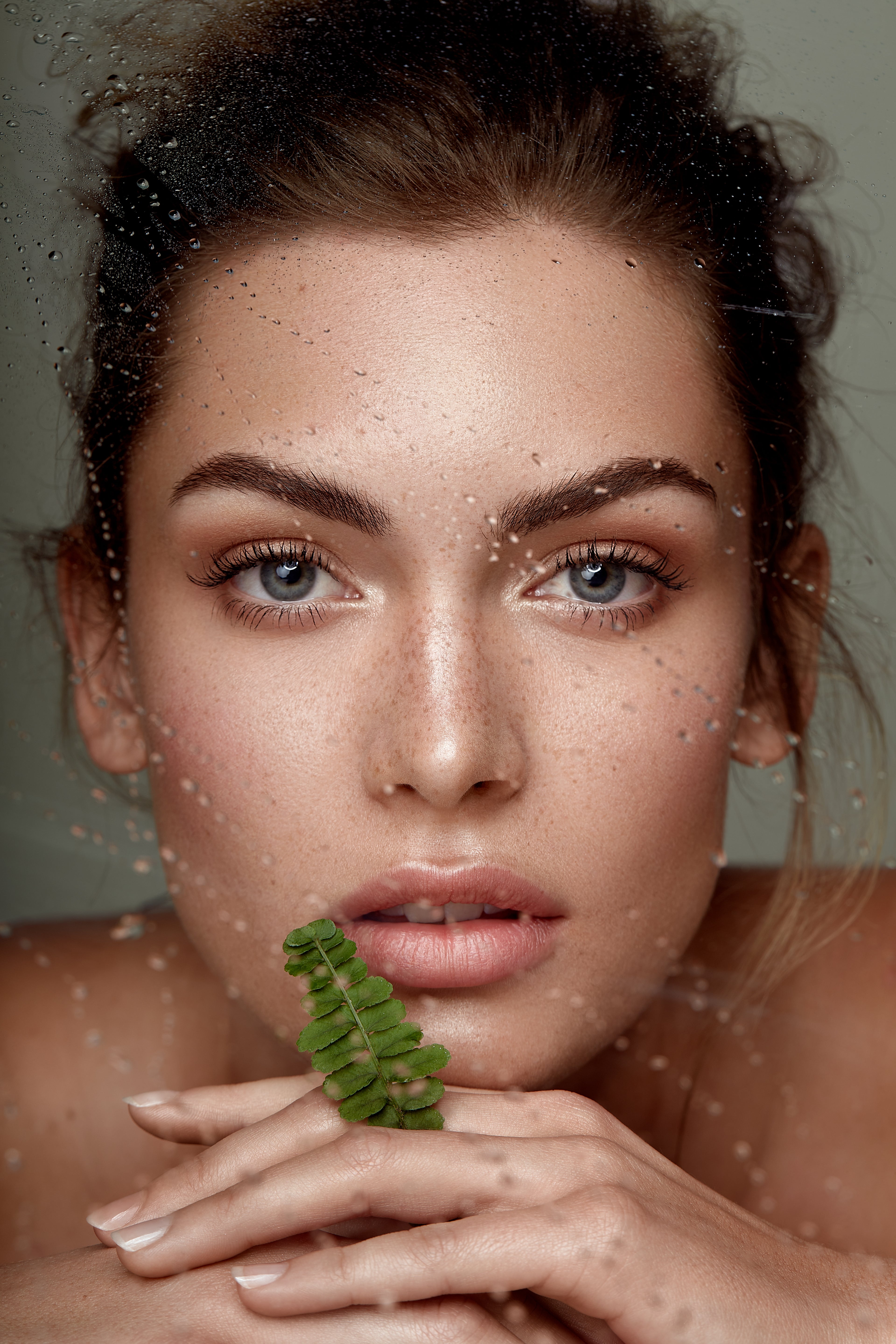 Frauengesicht hinter einer mit Regentropfen übersäten Glasscheibe