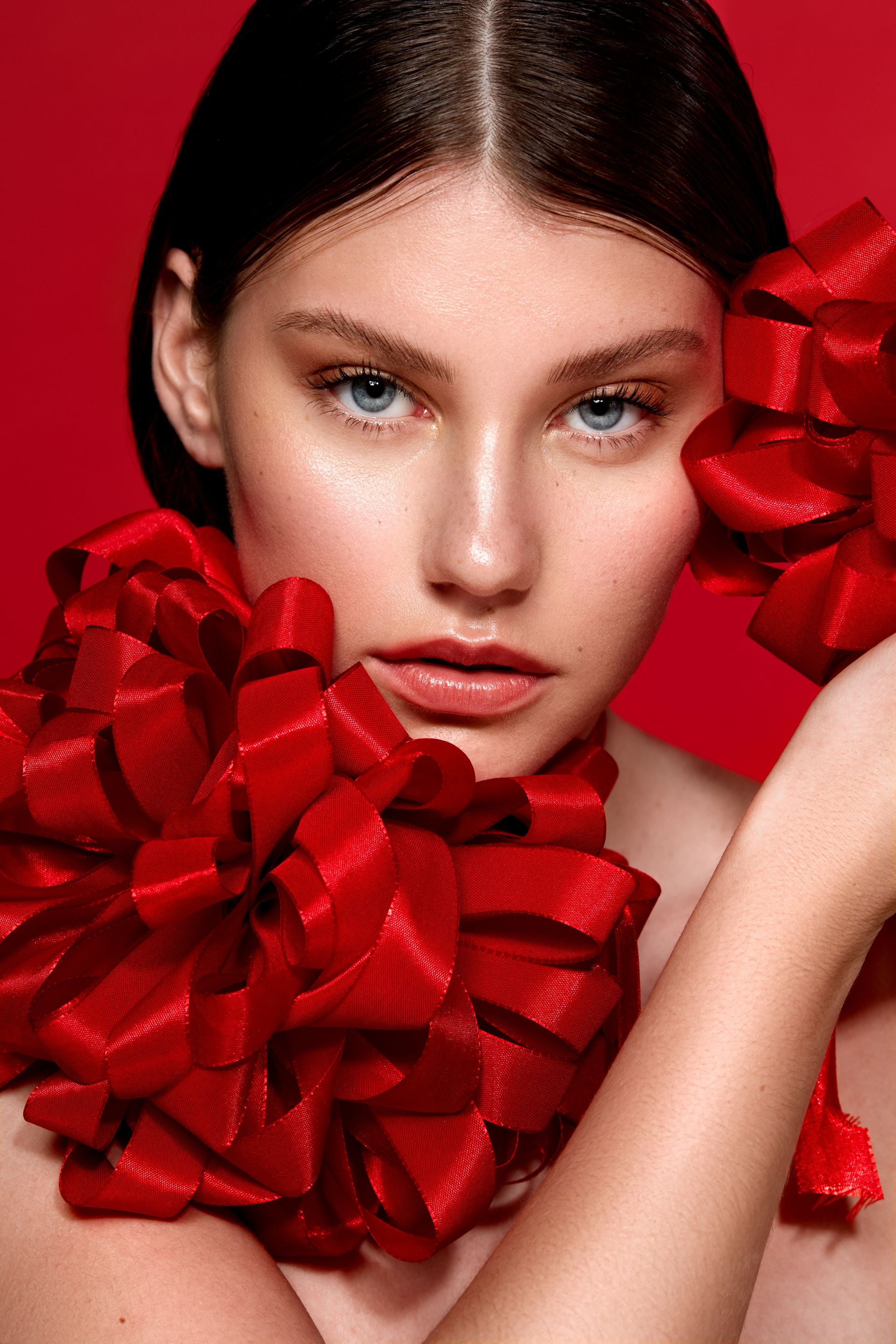 Model mit blauen Augen und dunklen Haaren mit roter Schleife